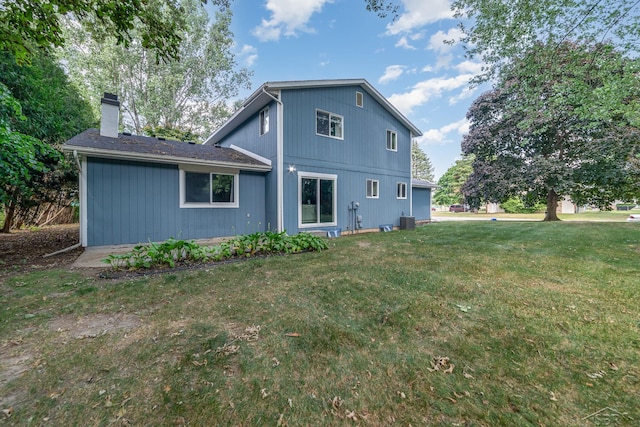 rear view of house featuring central AC unit and a lawn