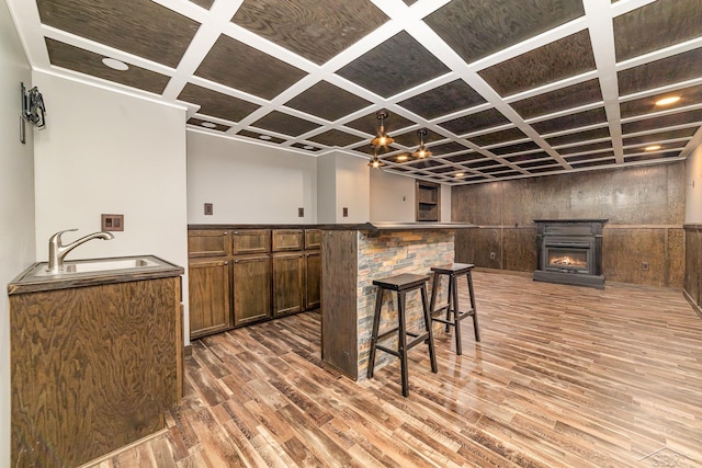 kitchen featuring a kitchen bar, coffered ceiling, sink, wood-type flooring, and a fireplace