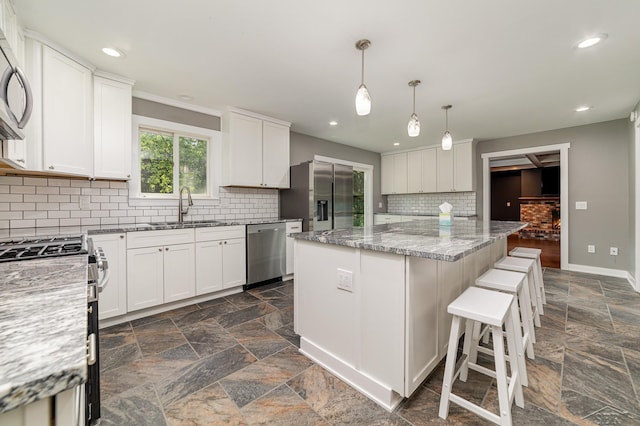 kitchen featuring light stone countertops, appliances with stainless steel finishes, sink, white cabinets, and a kitchen island