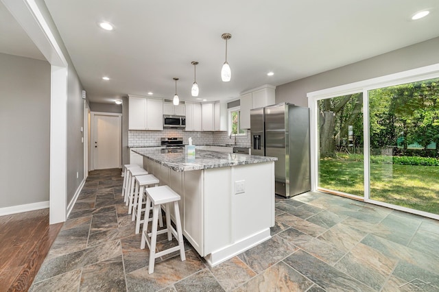 kitchen featuring white cabinetry, hanging light fixtures, backsplash, a kitchen island, and appliances with stainless steel finishes