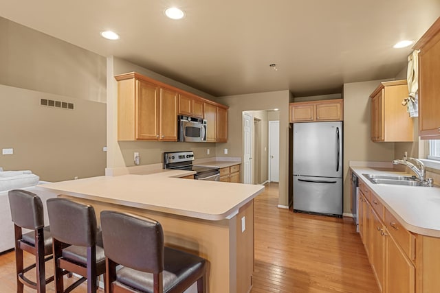 kitchen featuring kitchen peninsula, light wood-type flooring, a breakfast bar, stainless steel appliances, and sink