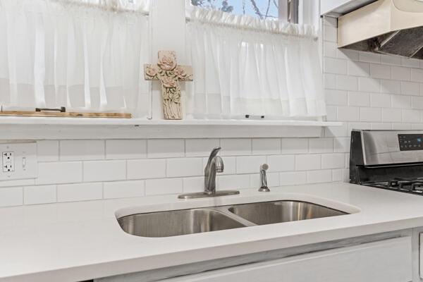 kitchen with sink, decorative backsplash, custom range hood, stainless steel range, and white cabinetry