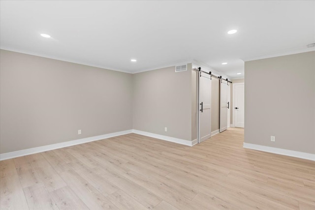 unfurnished room featuring a barn door, crown molding, and light wood-type flooring