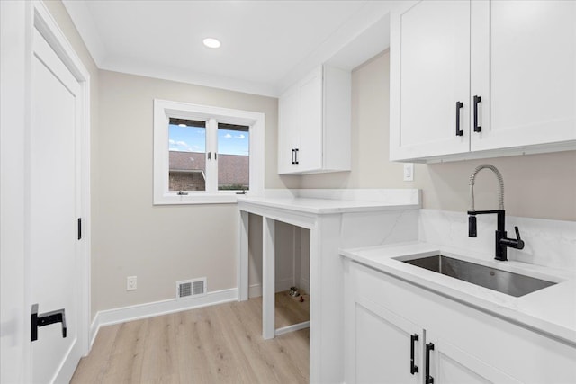 kitchen featuring light wood-type flooring, light stone counters, white cabinetry, and sink