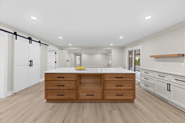 kitchen with ornamental molding, a barn door, white cabinets, a center island, and light hardwood / wood-style floors