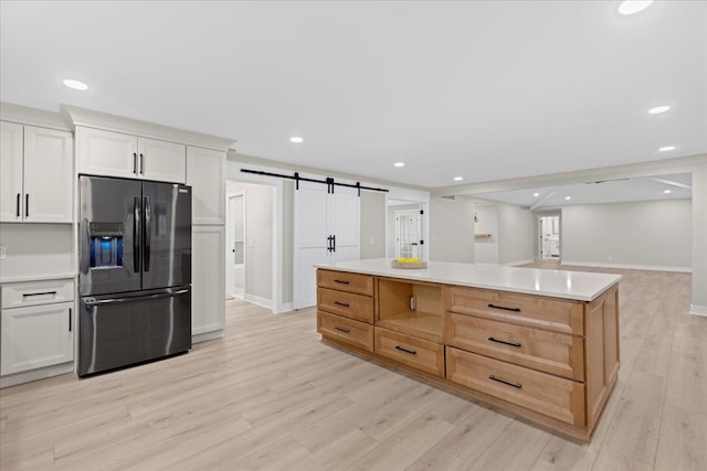 kitchen with stainless steel fridge, a barn door, light hardwood / wood-style flooring, and white cabinetry