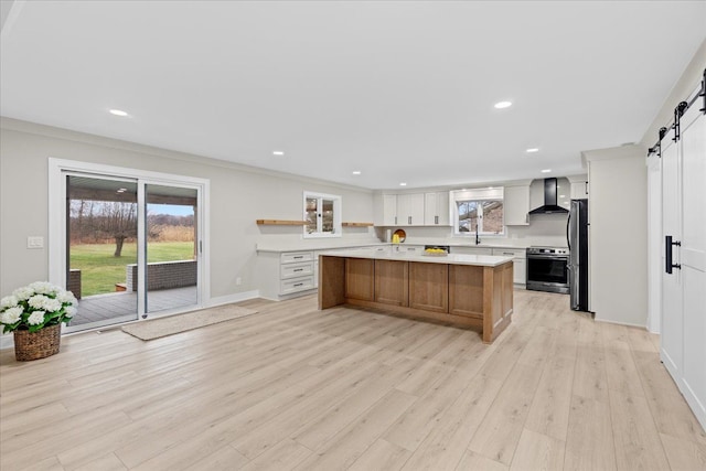 kitchen with white cabinetry, a large island, stainless steel appliances, wall chimney range hood, and a barn door