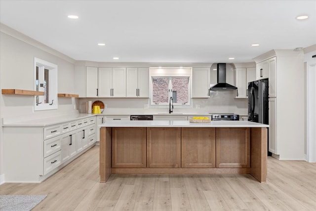 kitchen with white cabinets, light wood-type flooring, a center island, and wall chimney range hood