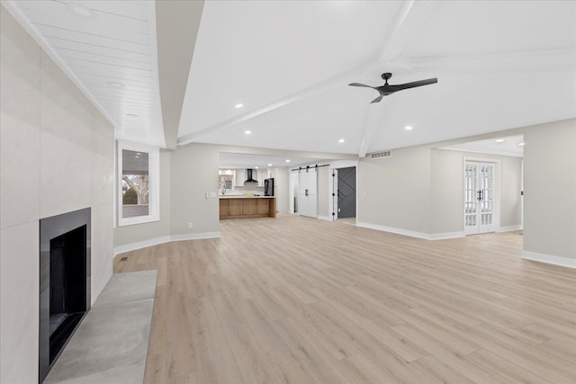 unfurnished living room with vaulted ceiling with beams, ceiling fan, a large fireplace, and light wood-type flooring