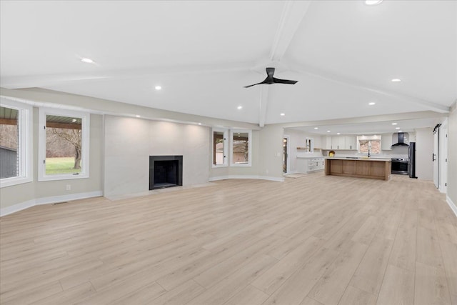 unfurnished living room with vaulted ceiling with beams, ceiling fan, light hardwood / wood-style flooring, and a fireplace