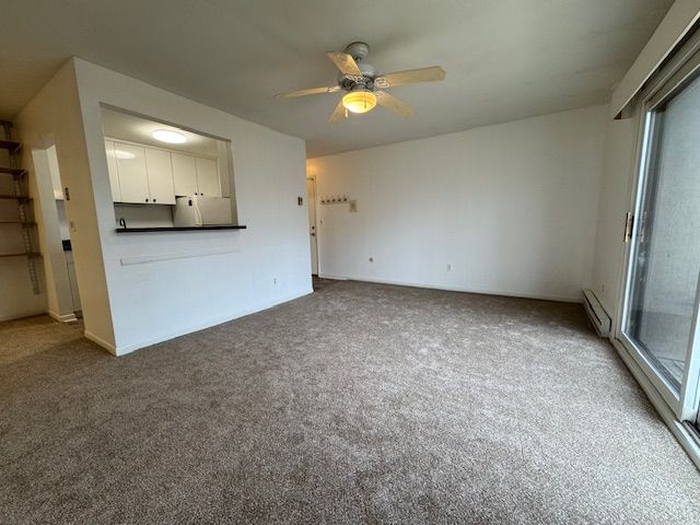 unfurnished living room featuring carpet flooring, ceiling fan, a wealth of natural light, and a baseboard radiator