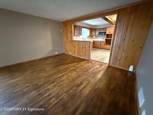 unfurnished living room with a textured ceiling, dark hardwood / wood-style flooring, beam ceiling, and wood walls