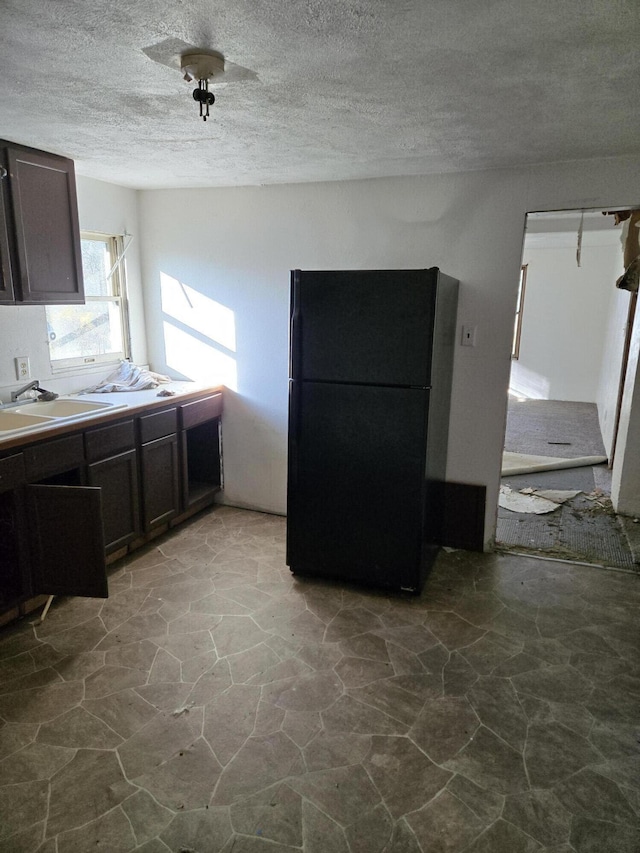 kitchen featuring black fridge, dark brown cabinets, a textured ceiling, and sink