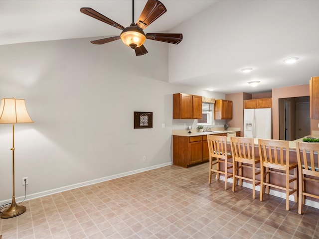 kitchen featuring ceiling fan, white fridge with ice dispenser, sink, vaulted ceiling, and a breakfast bar