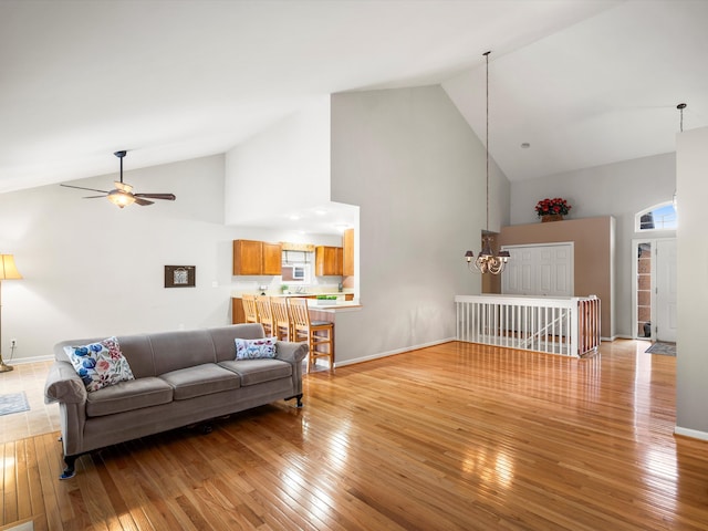 living room with ceiling fan with notable chandelier, high vaulted ceiling, and light hardwood / wood-style flooring