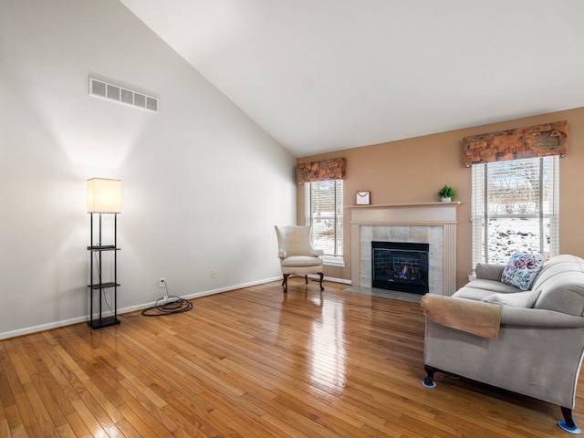 living room with a tiled fireplace, high vaulted ceiling, and light hardwood / wood-style flooring