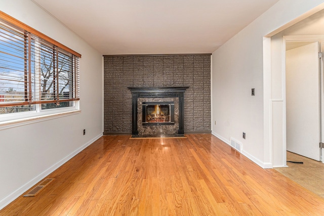 unfurnished living room with light wood-type flooring and a tiled fireplace