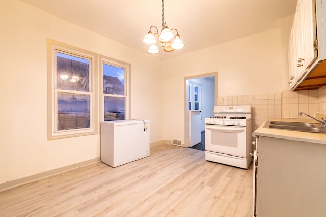 kitchen featuring refrigerator, sink, decorative light fixtures, a notable chandelier, and white range with gas cooktop