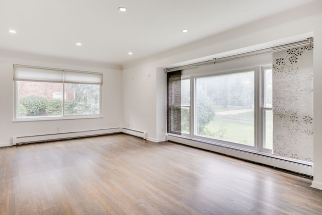 spare room featuring a baseboard heating unit, light hardwood / wood-style floors, and a healthy amount of sunlight