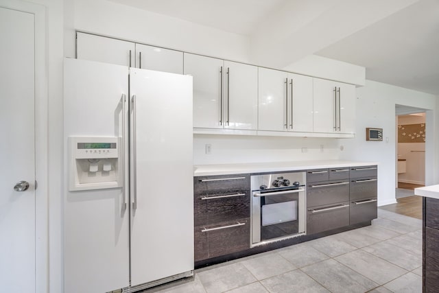 kitchen featuring white cabinets, oven, white fridge with ice dispenser, and light tile patterned floors