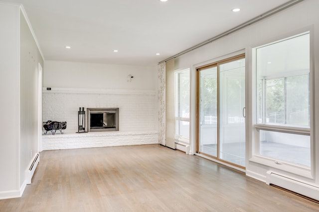 unfurnished living room with baseboard heating, a fireplace, plenty of natural light, and light hardwood / wood-style floors