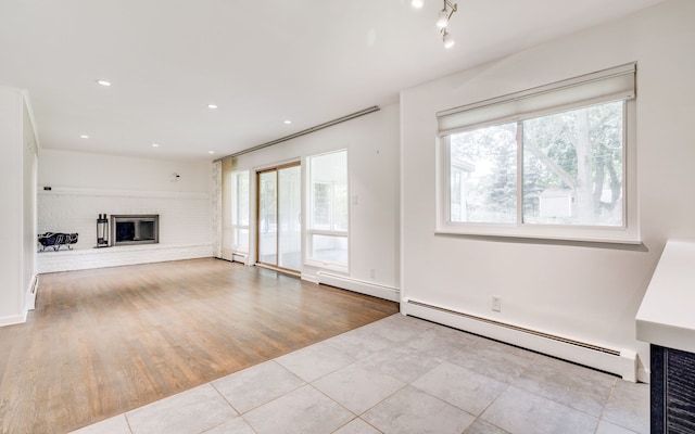 unfurnished living room featuring baseboard heating, plenty of natural light, light hardwood / wood-style floors, and a brick fireplace