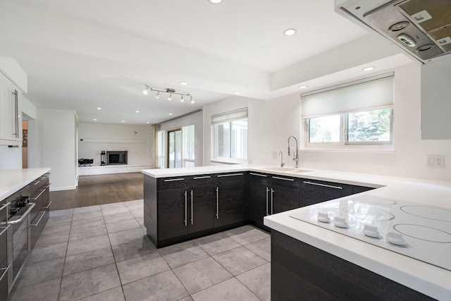 kitchen featuring sink, a brick fireplace, kitchen peninsula, light tile patterned flooring, and exhaust hood