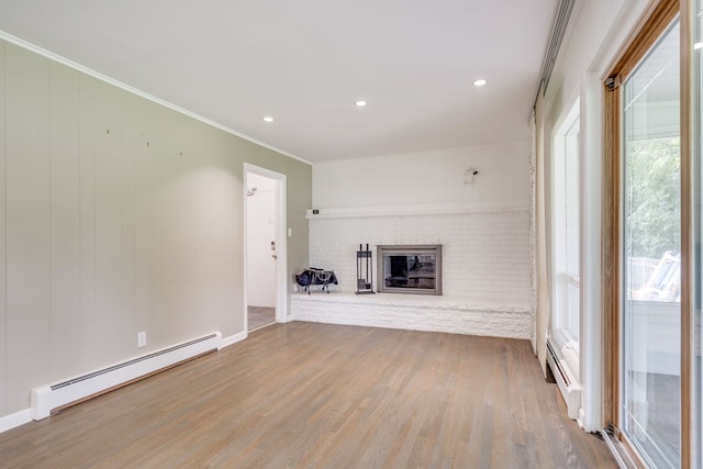 unfurnished living room with hardwood / wood-style flooring, ornamental molding, baseboard heating, and a brick fireplace