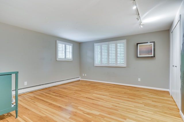 unfurnished room with track lighting, light hardwood / wood-style flooring, and a baseboard heating unit