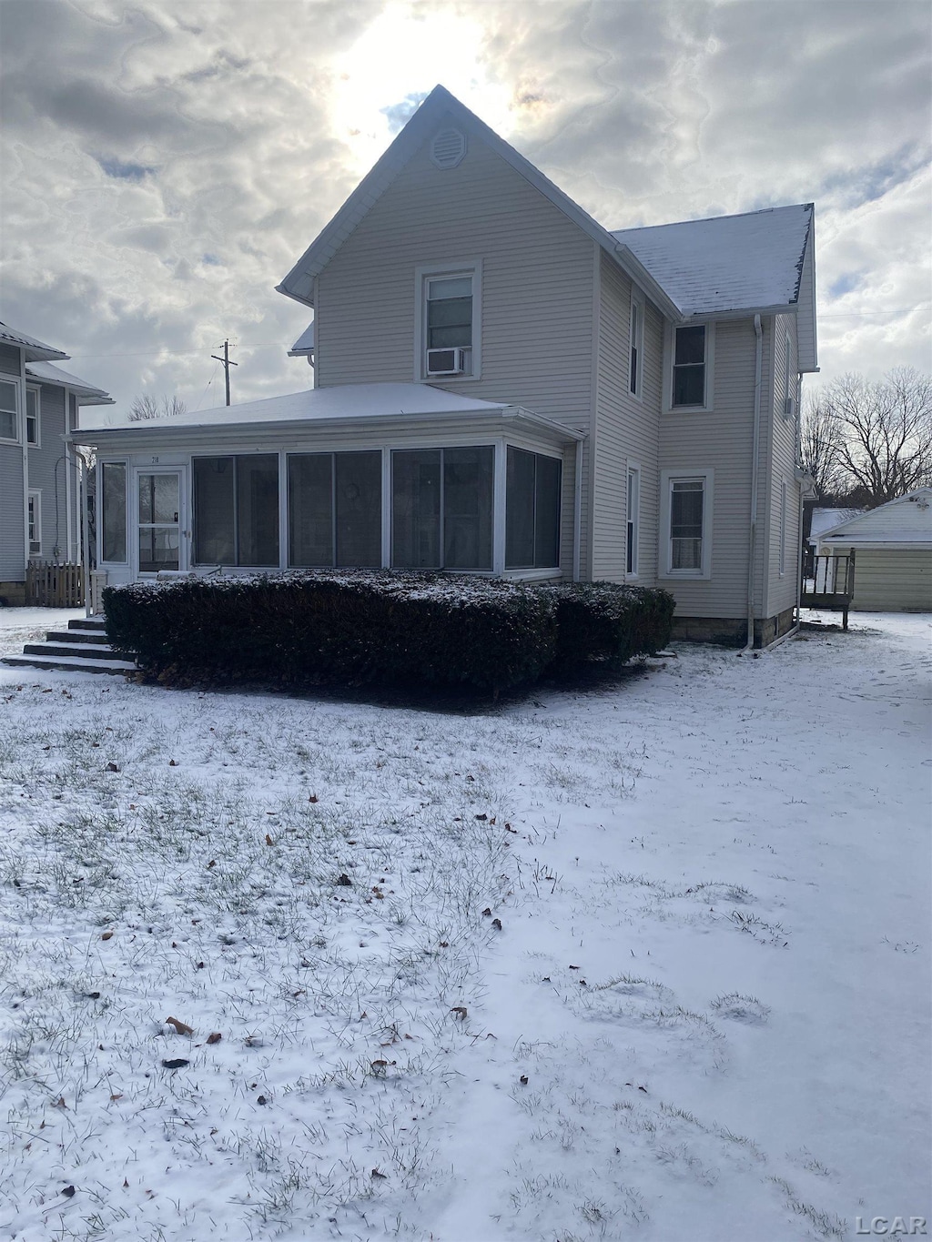 snow covered back of property with a sunroom