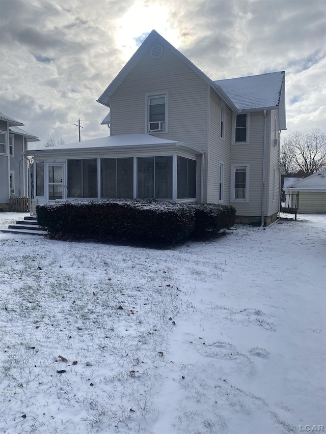 snow covered back of property with a sunroom