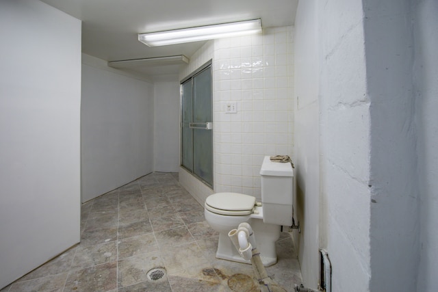 bathroom with tile walls, toilet, and a shower with door