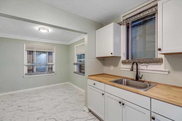 kitchen with wood counters, white cabinetry, and sink