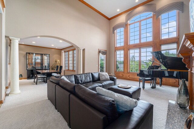 carpeted living room with a towering ceiling, crown molding, and ornate columns