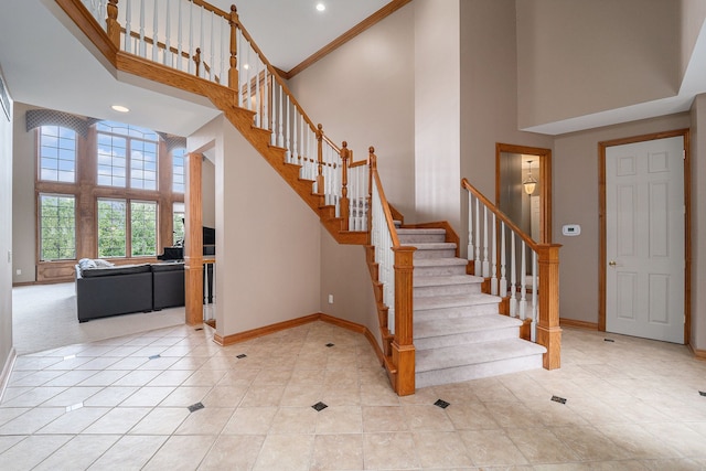 stairs with a towering ceiling, crown molding, and tile patterned floors