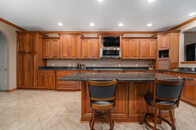 kitchen featuring a kitchen bar, dark stone countertops, and crown molding