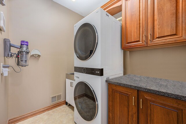 clothes washing area featuring stacked washing maching and dryer, light tile patterned flooring, and cabinets