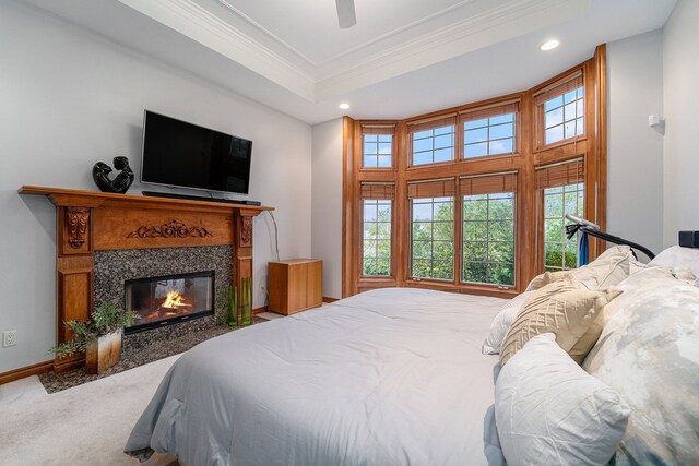 carpeted bedroom with ceiling fan, a raised ceiling, a tile fireplace, and crown molding