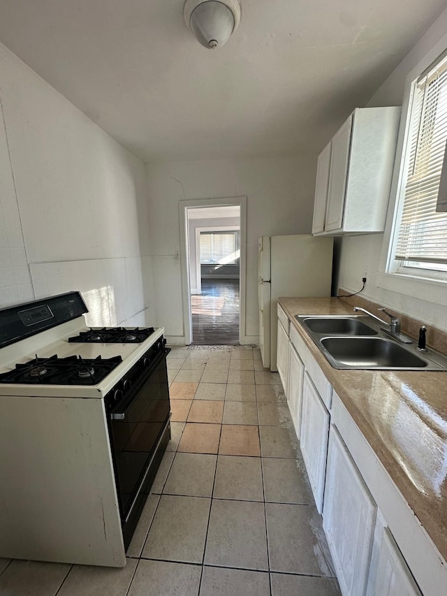 kitchen featuring white cabinetry, light tile patterned floors, white fridge, sink, and gas stove