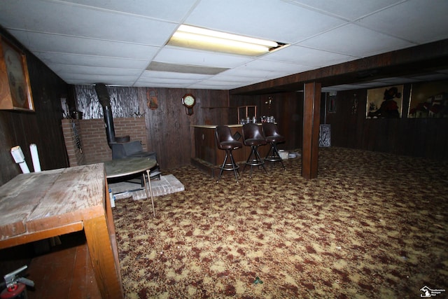 basement featuring carpet flooring, a paneled ceiling, and wooden walls