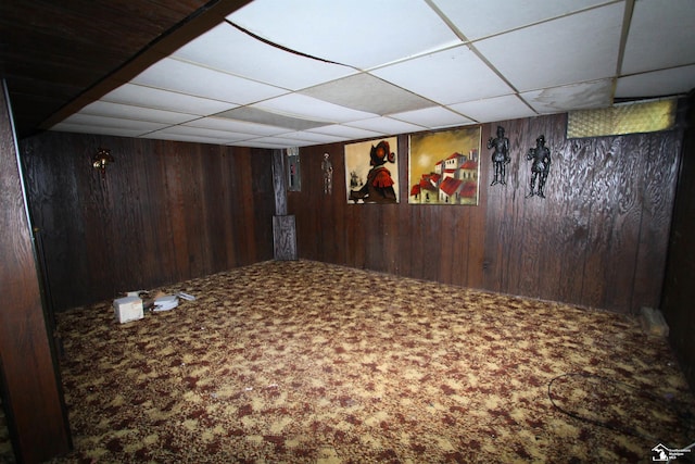 basement featuring a drop ceiling, wood walls, and carpet floors