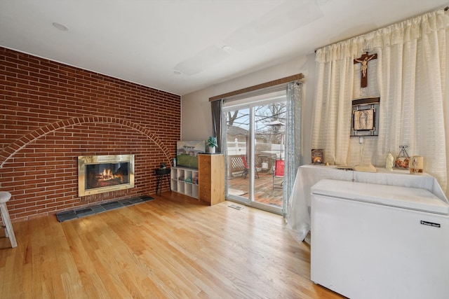 unfurnished living room featuring light wood-type flooring, brick wall, and a brick fireplace