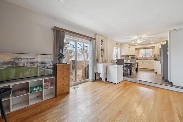 kitchen featuring light hardwood / wood-style flooring, ceiling fan, stainless steel fridge, tasteful backsplash, and white cabinetry