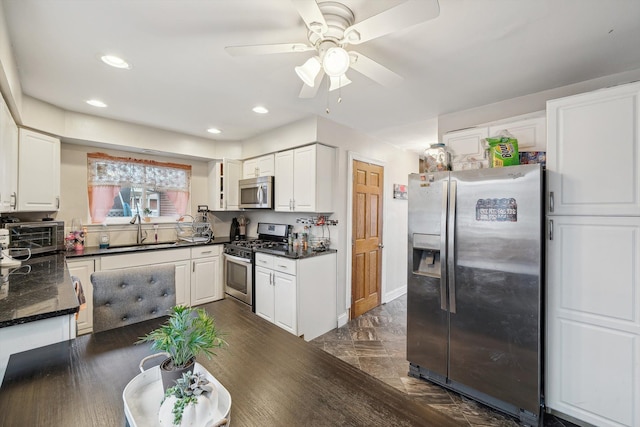 kitchen with dark stone counters, white cabinets, sink, ceiling fan, and appliances with stainless steel finishes