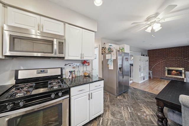 kitchen with ceiling fan, dark stone countertops, a fireplace, white cabinetry, and stainless steel appliances