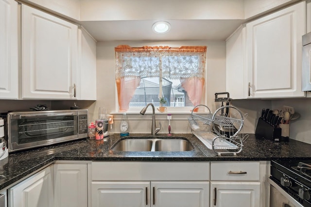 kitchen with dark stone countertops, white cabinetry, sink, and white range with gas stovetop