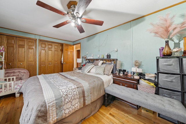 bedroom featuring ceiling fan, ornamental molding, two closets, and hardwood / wood-style flooring