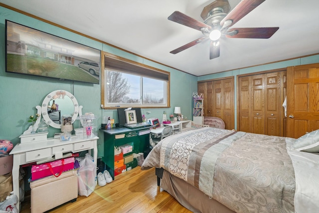 bedroom with ceiling fan, light hardwood / wood-style floors, ornamental molding, and multiple closets