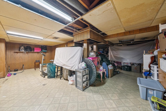 basement featuring a drop ceiling and wood walls