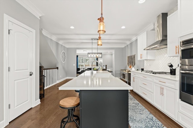 kitchen with white cabinets, a kitchen island with sink, wall chimney exhaust hood, and pendant lighting